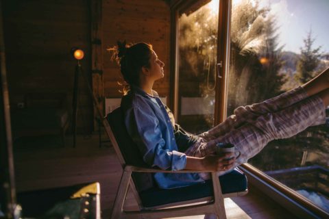 A woman reclines with her feet up in the morning sunrise with a cup of coffee to represent financing a vacation home