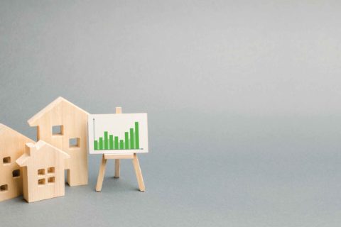 Wooden cutouts of houses next to a graph represent market trends for spring 2021