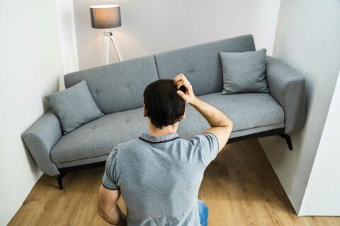 A person scratches their head looking at a huge couch that doesn't fit into a small space to represent staging a small space