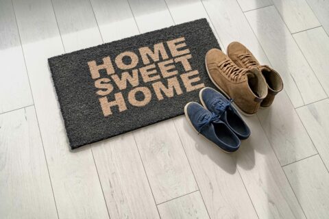 Two sets of shoes on a welcome mat that says "Home Sweet Home". Welcome Mats are a great gift for your old home's new owners.