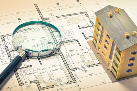 A model home on plans with a magnifying glass to signify pre-construction purchase